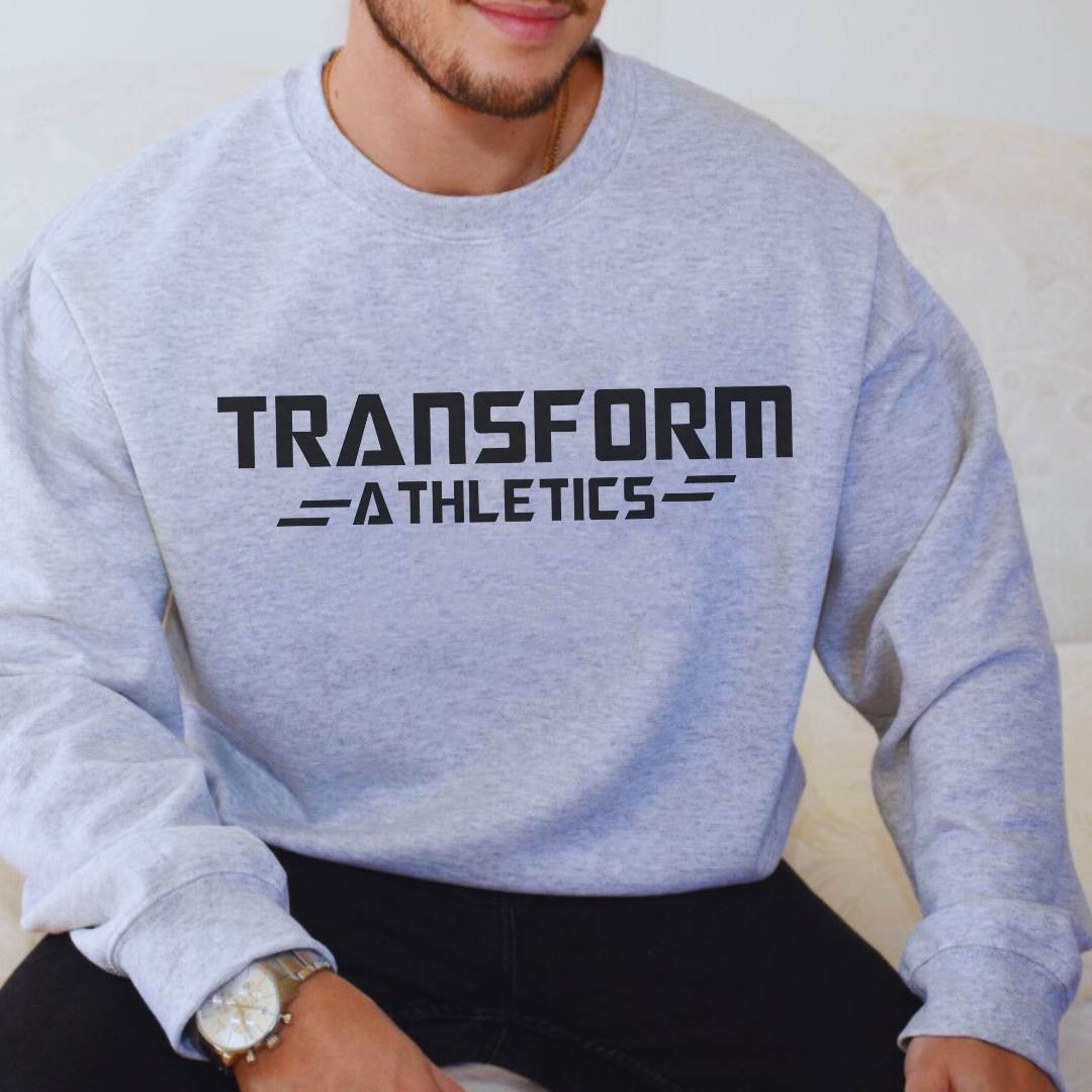 man sitting while modeling the heather light gray adult fleece pullover with "Transform Athletics" in black across the front